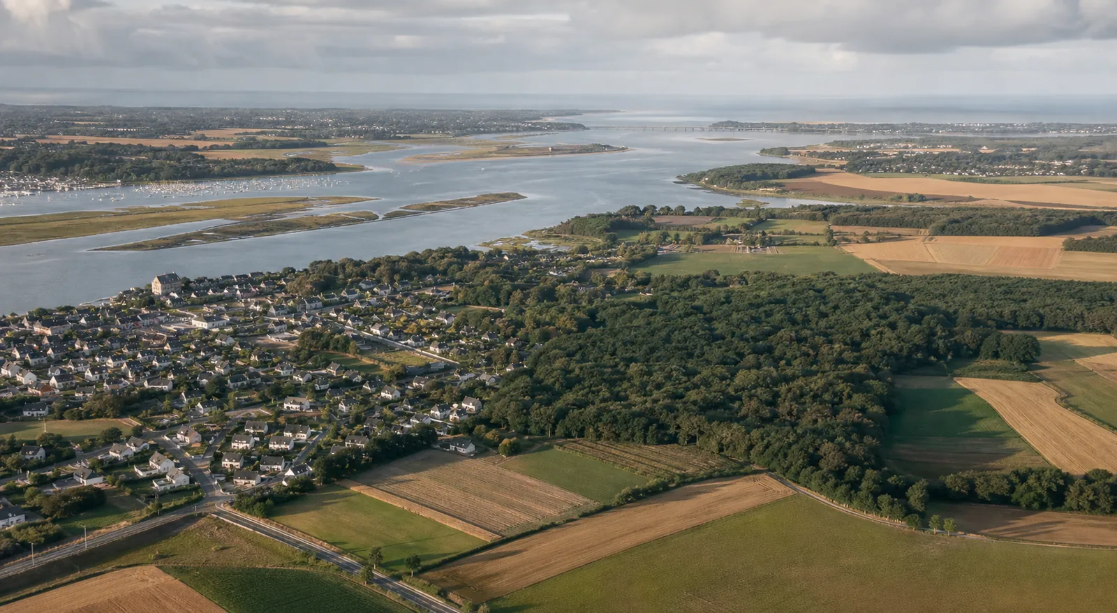 Territoire habité entre terres agricoles, bois, ville et étendue d’eau.