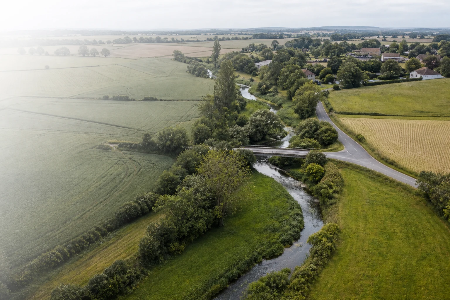 Territoire rural où un cours d’eau, une route, un pont, des parcelles et un village forment un réseau de relations spatiales.