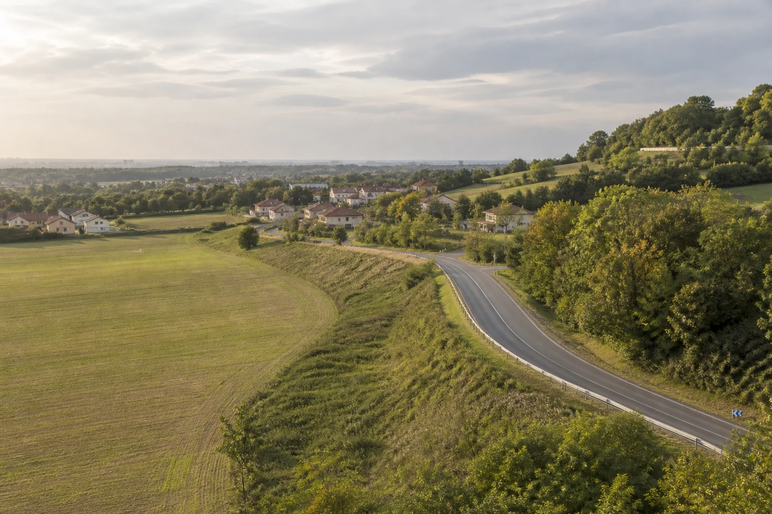 Territoire habité réunissant une route, un talus, des parcelles, de la végétation et des bâtiments.